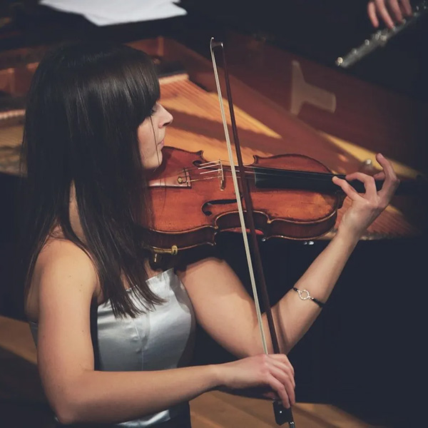 Woman playing a violin next to a grand piano